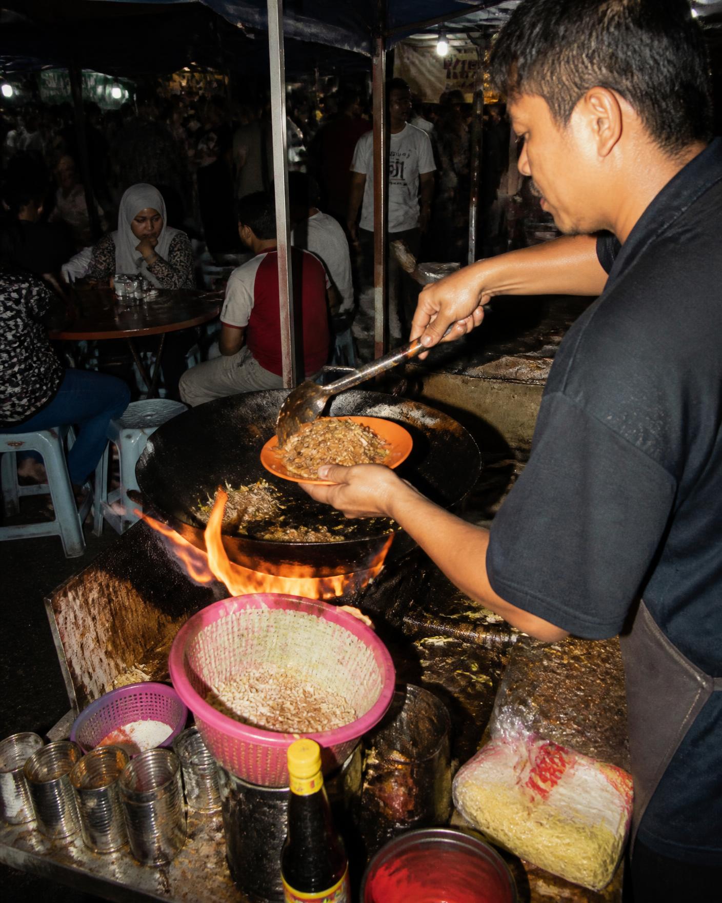 Hawker cooking char kuey teow over open flame at a Malaysian night market