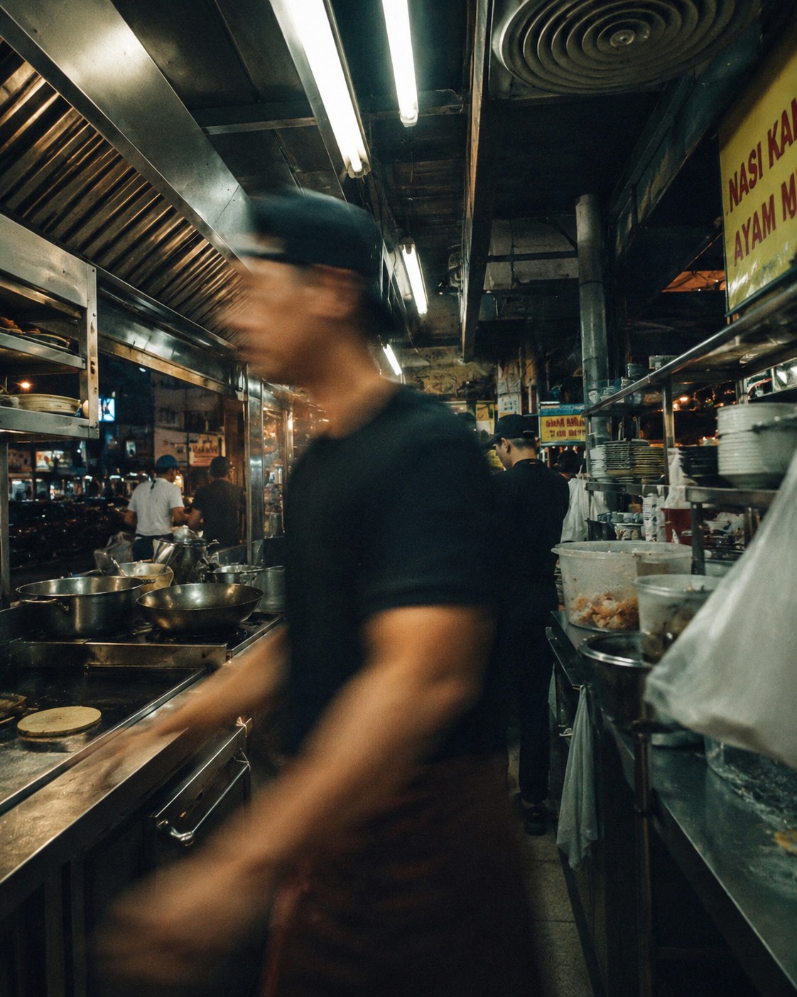 Suasana dapur kedai makan tempatan di Malaysia dengan pekerja sedang bergerak laju menyiapkan pesanan